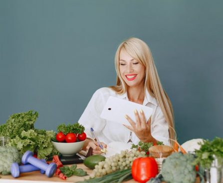 Woman using a tablet surrounded by fresh vegetables at a table, showcasing healthy lifestyle and technology.