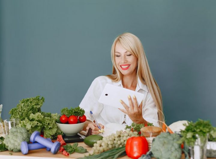 Woman using a tablet surrounded by fresh vegetables at a table, showcasing healthy lifestyle and technology.