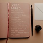 Open notebook with 2021 goals, calligraphy pen, envelope, and ink jar on neutral background.