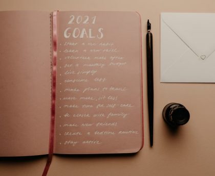 Open notebook with 2021 goals, calligraphy pen, envelope, and ink jar on neutral background.