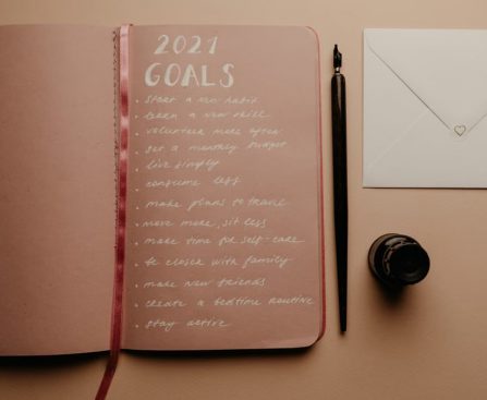 Open notebook with 2021 goals, calligraphy pen, envelope, and ink jar on neutral background.
