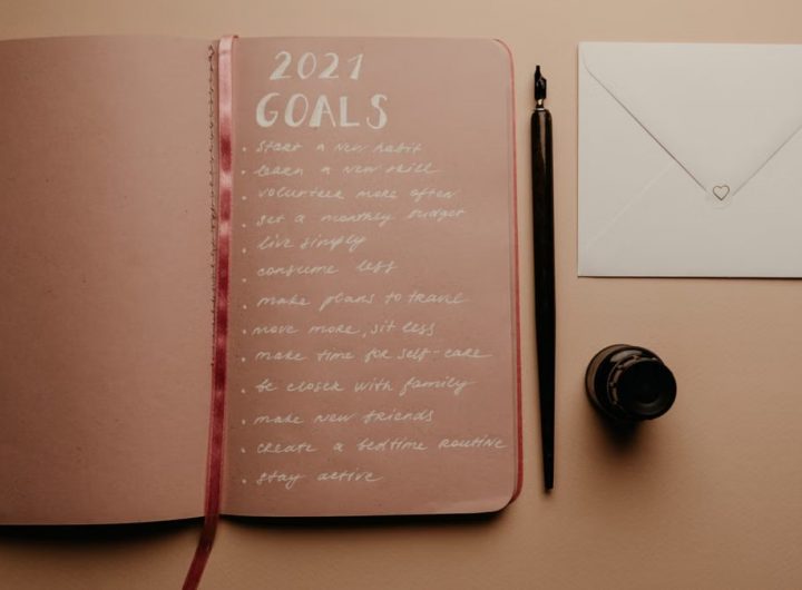 Open notebook with 2021 goals, calligraphy pen, envelope, and ink jar on neutral background.