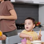 Two young boys enjoying their breakfast in a modern kitchen setting with their mother nearby.