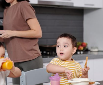 Two young boys enjoying their breakfast in a modern kitchen setting with their mother nearby.