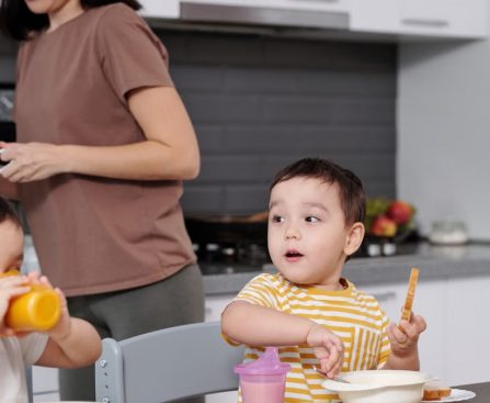 Two young boys enjoying their breakfast in a modern kitchen setting with their mother nearby.