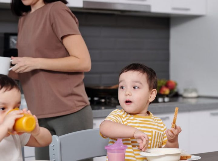 Two young boys enjoying their breakfast in a modern kitchen setting with their mother nearby.
